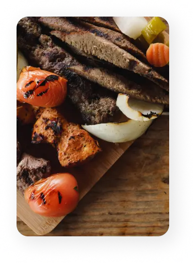 Close-up of mixed grilled kabobs including lamb gyro, chicken, and beef with roasted tomatoes and onions, served on a wooden board at Aladdin Mediterranean Cuisine in Houston.