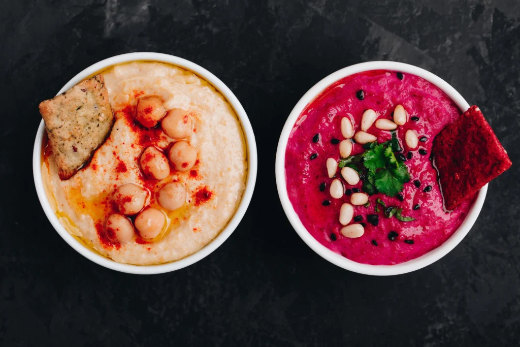 Classic hummus and vibrant beetroot hummus topped with pine nuts and herbs, highlighting the health benefits of Mediterranean food. Food and Mood, benefits of Lebanese cuisine.