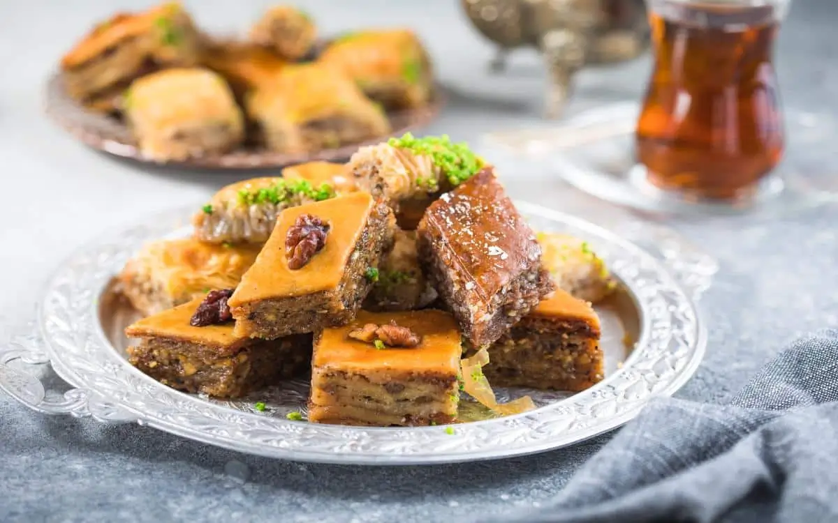 Delicious piece of baclawa on a golden plate, topped with pistachios and drizzled with honey.