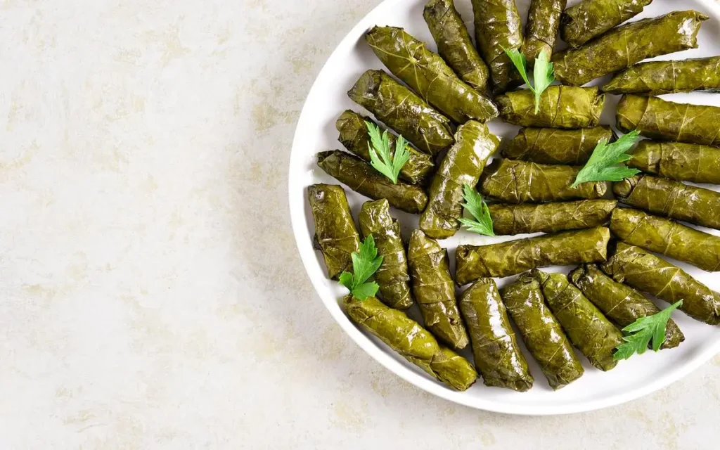 A plate of traditional Mediterranean dolmas, stuffed grape leaves filled with rice and herbs, garnished with fresh parsley.