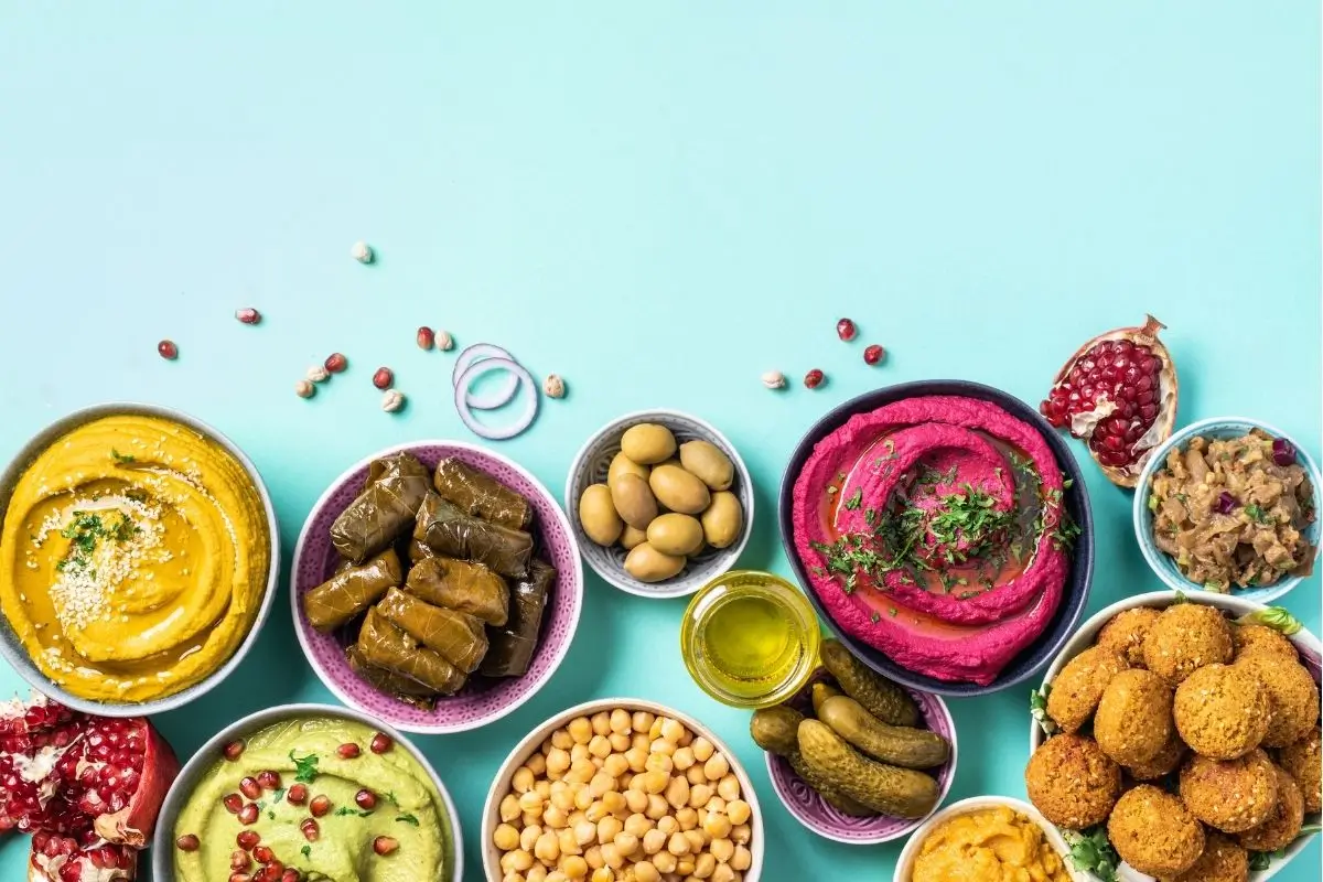 Healthy Mediterranean Food in Houston mezze bowls—hummus, beet dip, dolmas, chickpeas, olives & falafel—on a light‑blue surface.